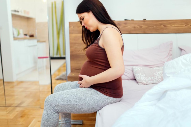 b2ap3 large pregnant woman sat on bed holding bump experiencing vaginal pain