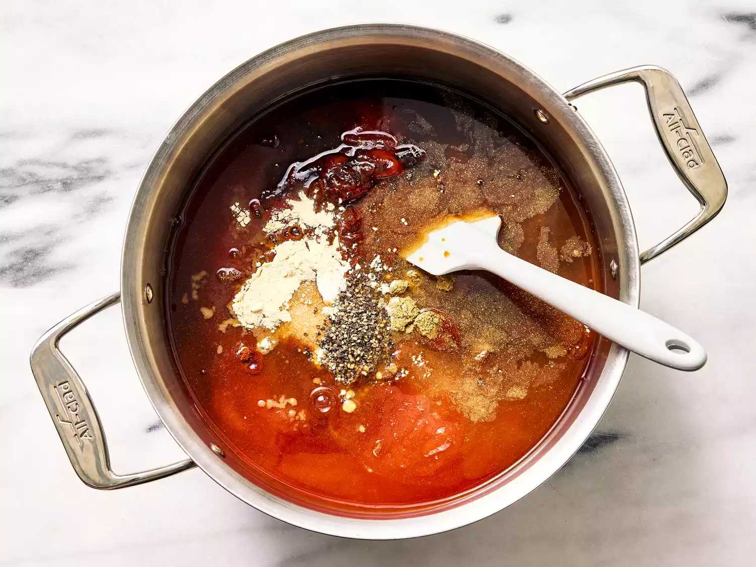 یک قابلمه حاوی مواد طرز تهیه سس باربیکیو، شامل ادویه ها و محصولات گوجه فرنگی، به همراه یک کفگیر برای مخلوط کردن